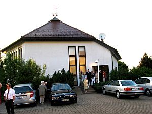 Neuapostolische Kirche in Kleinengstingen. Autos vor der Kirche und Personen kommen aus der Kirche heraus.