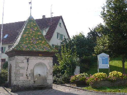 Kleinengstinger Sauerbrunnen mit Bäumen und einem Haus im Hintergrund