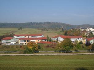 Waldorfschule auf der Alb​ aus weiterer Entfernung. Im Vorder- und Hintergrund sind Wiesen und Bäume.